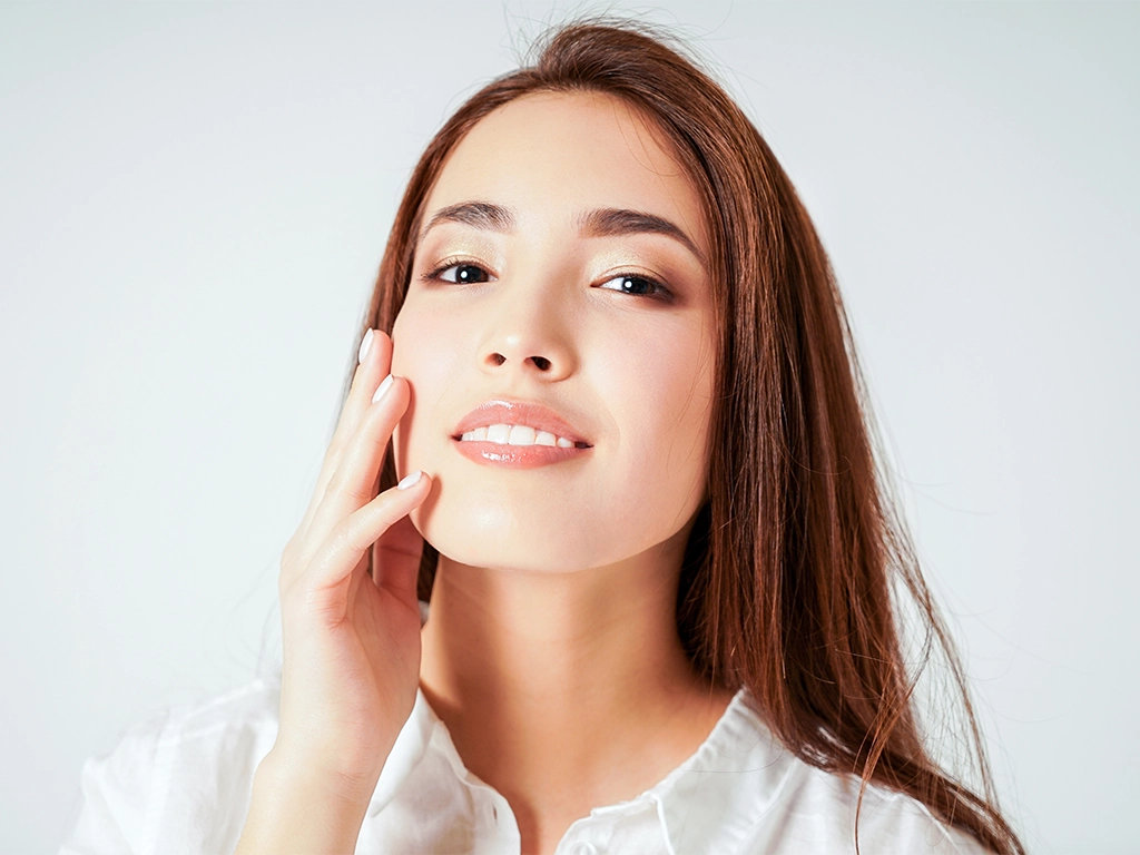 Smiling young woman touching her face gently while showing a bright, attractive smile